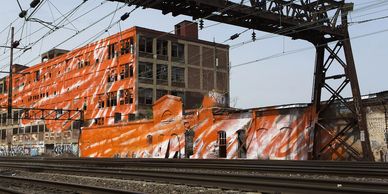 Orange and white spray paint covers multiple stories of an abandoned warehouse. 