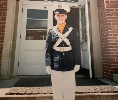 Young cadet in uniform standing on steps outside a building.