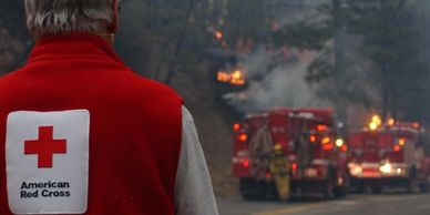 Back view of a Red Cross volunteer near firefighters as they actively extinguish a large blaze.