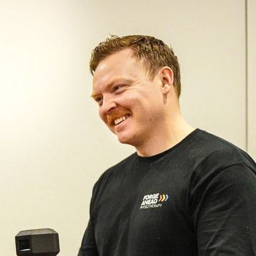 Smiling man in a black shirt holding a dumbbell.