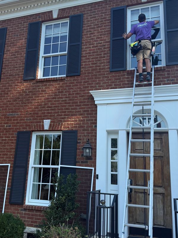 Person cleaning second-story window on brick house.