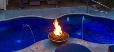 A stylish backyard pool with blue lighting and a central fire pit.