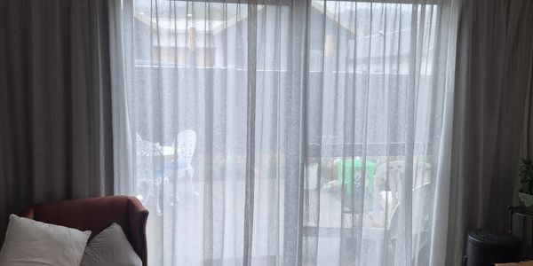 Sheer curtains covering a window with a red chair nearby.