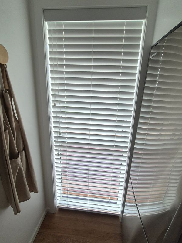 Window with vertical blinds partially open, reflecting on a shiny surface.
