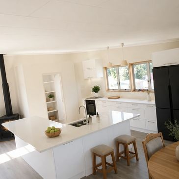 Bright modern kitchen with white countertops and wooden stools.