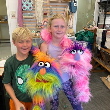 Two children holding colorful furry puppets and smiling.