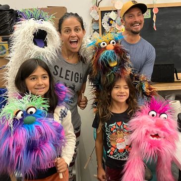 A family joyfully posing with colorful, fluffy puppets indoors.
