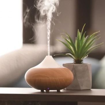 A wooden essential oil diffuser releasing mist beside a small potted plant.