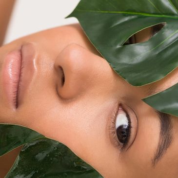 Close-up of a woman's face with green leaves partially covering it.