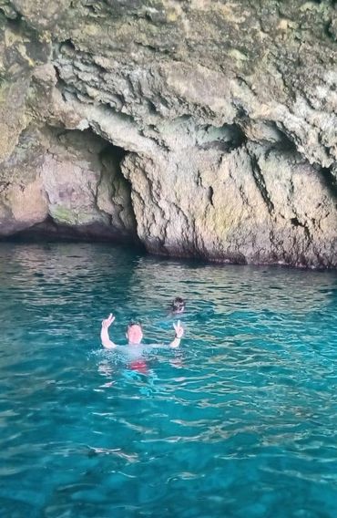 People swimming in clear blue water near a rocky cave.