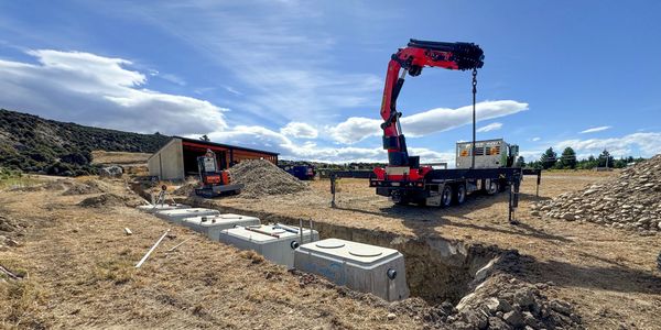 Construction site with heavy machinery and underground concrete tanks under a partly cloudy sky.