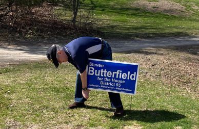 A man sets up a political campaign sign for Steven Butterfield outdoors.
