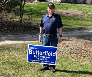 Man standing outdoors holding a political campaign sign for Steven Butterfield.