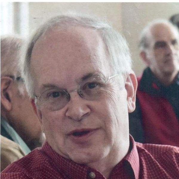 Elderly man with glasses speaking in a casual setting.