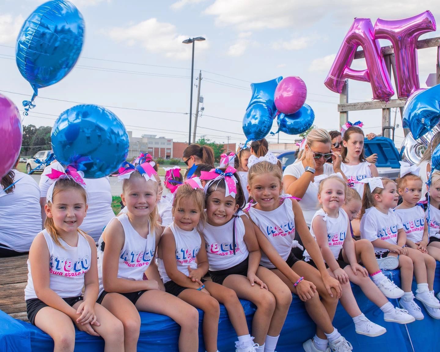 Young cheerleaders in matching outfits with balloons at an outdoor event.