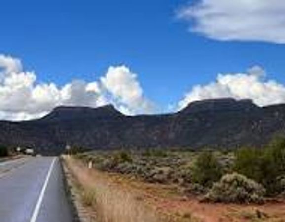 Desert road with flat-topped mountains under blue sky.
