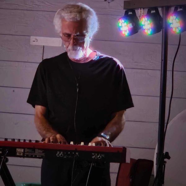 Elderly man with white hair and glasses illuminated by colorful lights.