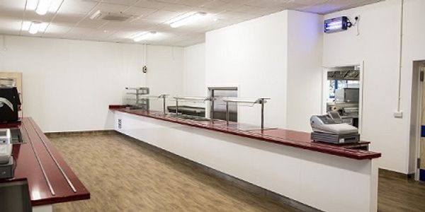 Two long school canteen servery counters with red surface and a till at the end