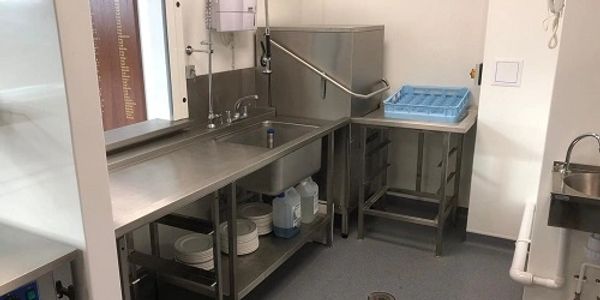 Corner wash up area of a commercial kitchen with hood dishwasher and sink