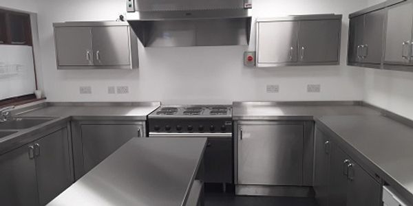 A centre island for preparing food- surrounded by stainless steel cupboards, cooker and extractor