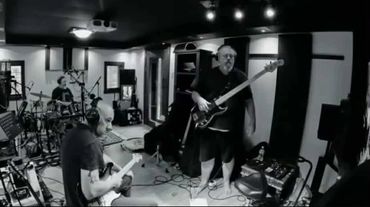 Three musicians play instruments in a recording studio, captured in black and white.