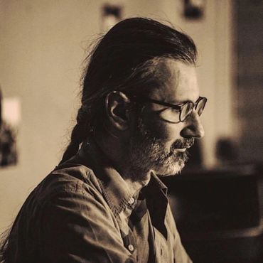 Profile of a man with glasses and a braided ponytail in warm lighting.