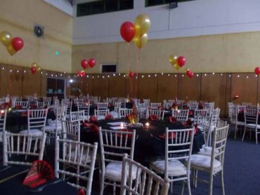 Decorated party hall with tables, chairs, and balloons.