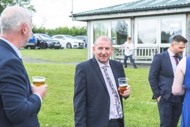 Men in suits holding beer outdoors.