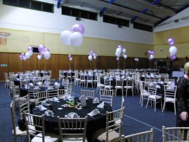 Event hall decorated with balloons and round tables.