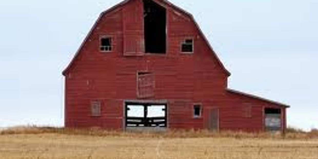 Old red barn with multiple open and closed windows in a field.