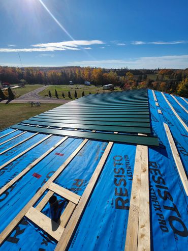 Sunlit roof under construction with blue waterproofing and green metal sheets.