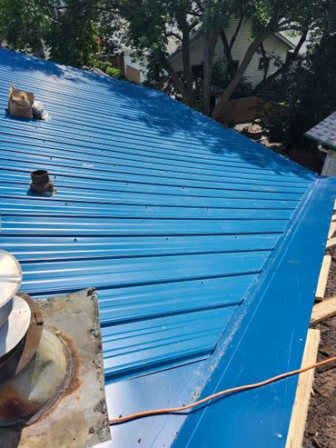 Shiny blue metal roof with trees and houses in the background.