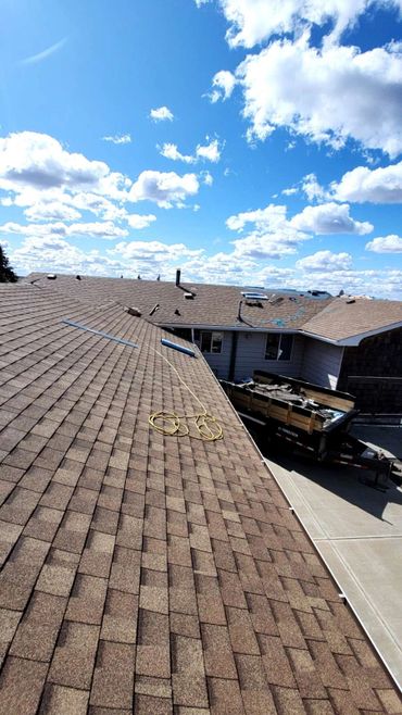 A brown shingled roof under a sky with scattered clouds and a trailer below.