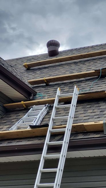 Ladders and wooden planks on a steep shingled roof during overcast weather.