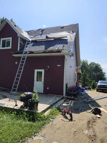 House roof repair in progress with ladders and tools outside.