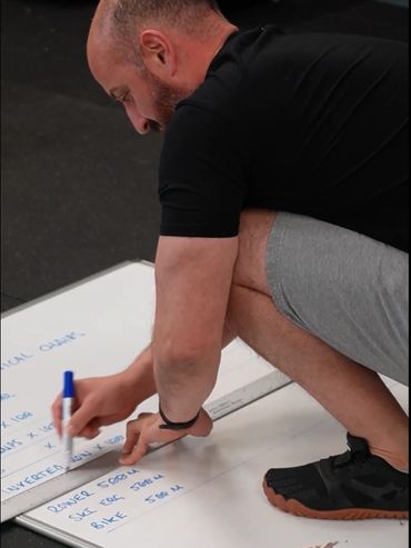 Man writing workout exercises on a whiteboard while squatting.