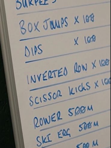 Whiteboard with a workout routine listing various exercises and distances.