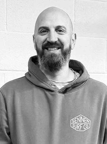 Smiling man with a beard wearing a hoodie with a surf company logo.