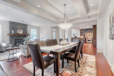 Modern dining room with leather chairs and an open living area featuring a stone fireplace.