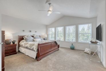 Bright bedroom with wooden bed and large windows overlooking trees.
