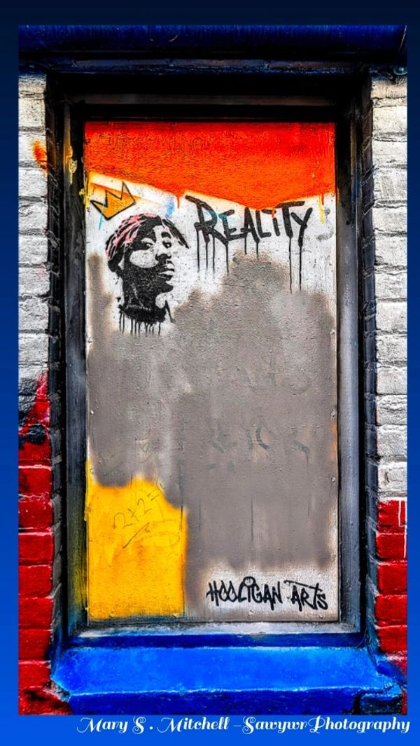 Street art with a portrait, crown, and the word 'REALITY' on a colorful wall.