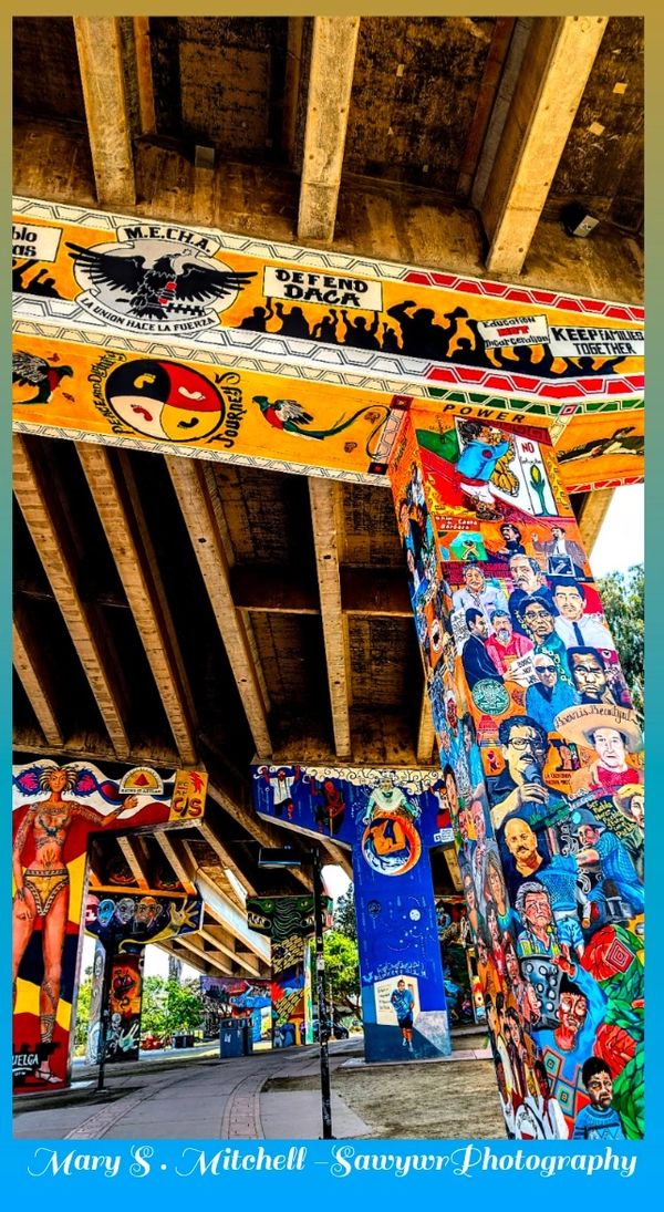 Colorful murals adorn freeway pillars under an urban bridge.