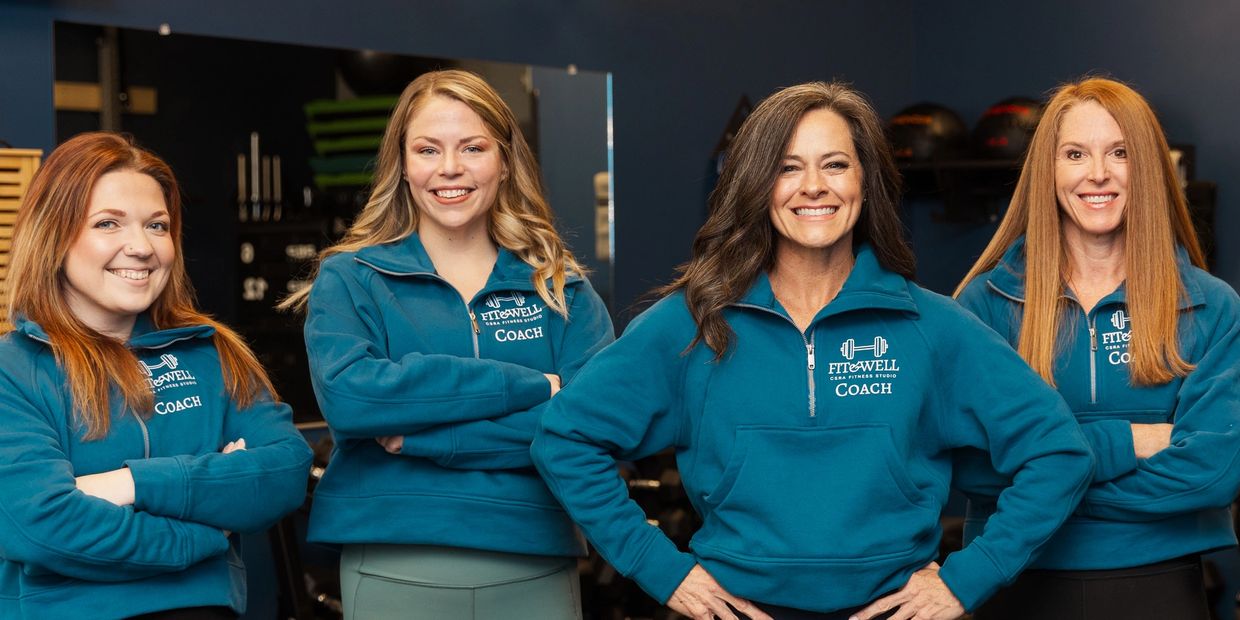 Four women fitness coaches smiling confidently in teal Fit & Well jackets.