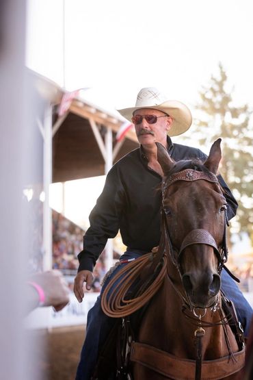 Man in a cowboy hat riding a horse at an outdoor event.