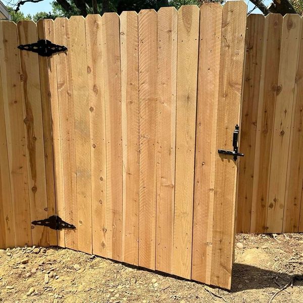 Newly installed wooden fence gate with black metal hinges and latch.
