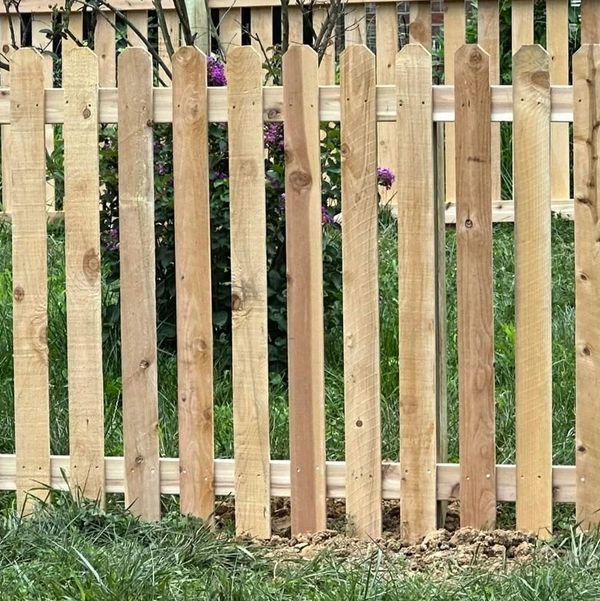 A wooden picket fence with fresh soil and grass in front.