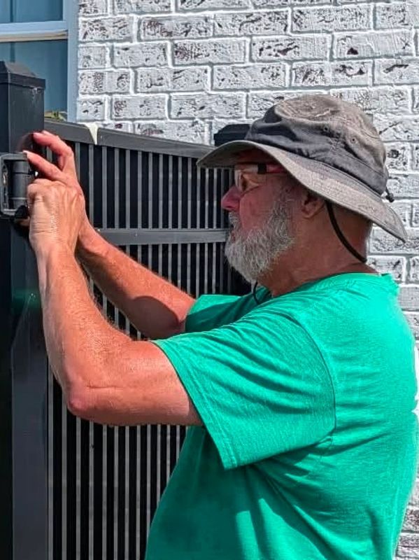 Fence repair specialist in Newburgh, Indiana adjusts gate hardware on an aluminum fence.