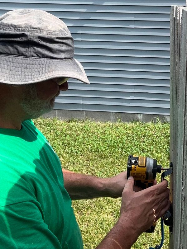 Ronald Willis, fence professional at Willis Outdoors LLC, repairs a gate on a wood privacy fence