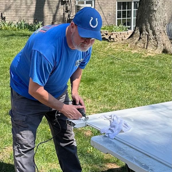 Man in blue shirt and cap working on a white panel outdoors.