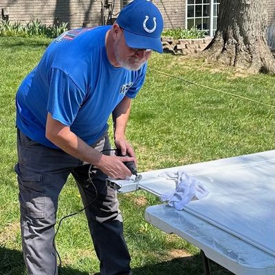 Man in blue shirt and cap sanding a white door outdoors.